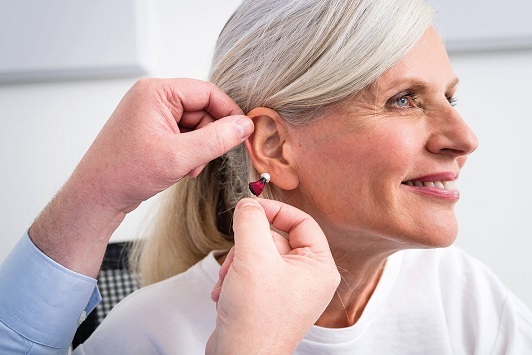 Seniorin bekommt ein modernes Hörgerät ins Ohr eingesetzt, Hörakustik Beratung.